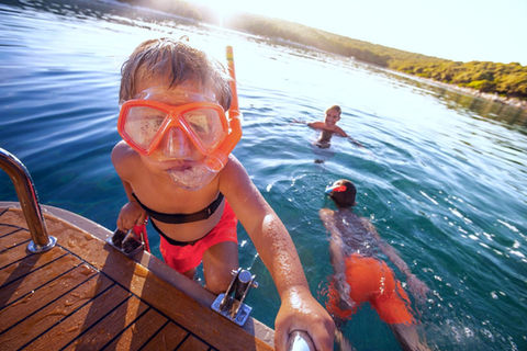 young boys are swimming near their yacht 